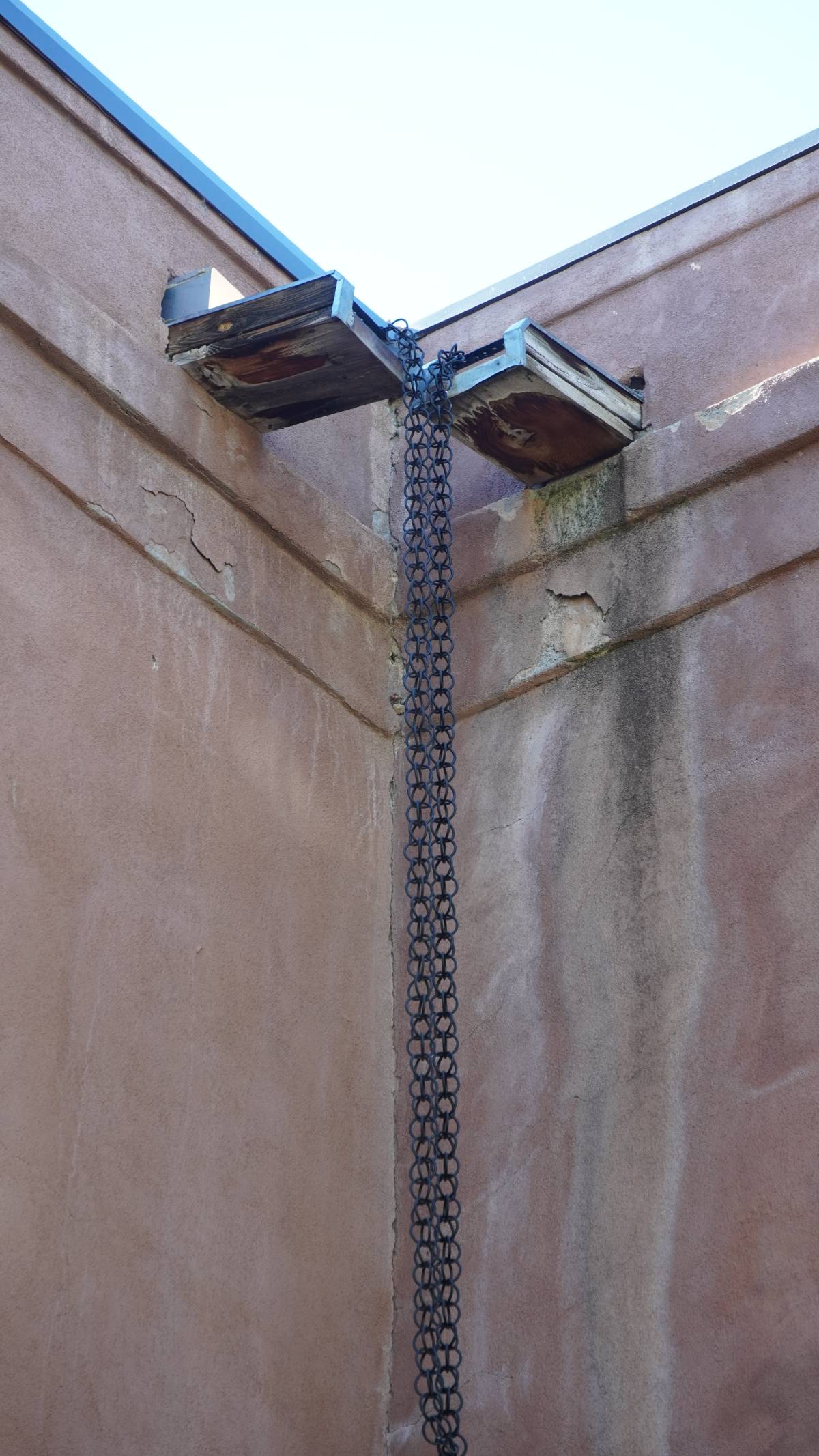 Rain chains hang from canales to direct runoff to the garden. The damage from undirected water flow is visible on the walls. 